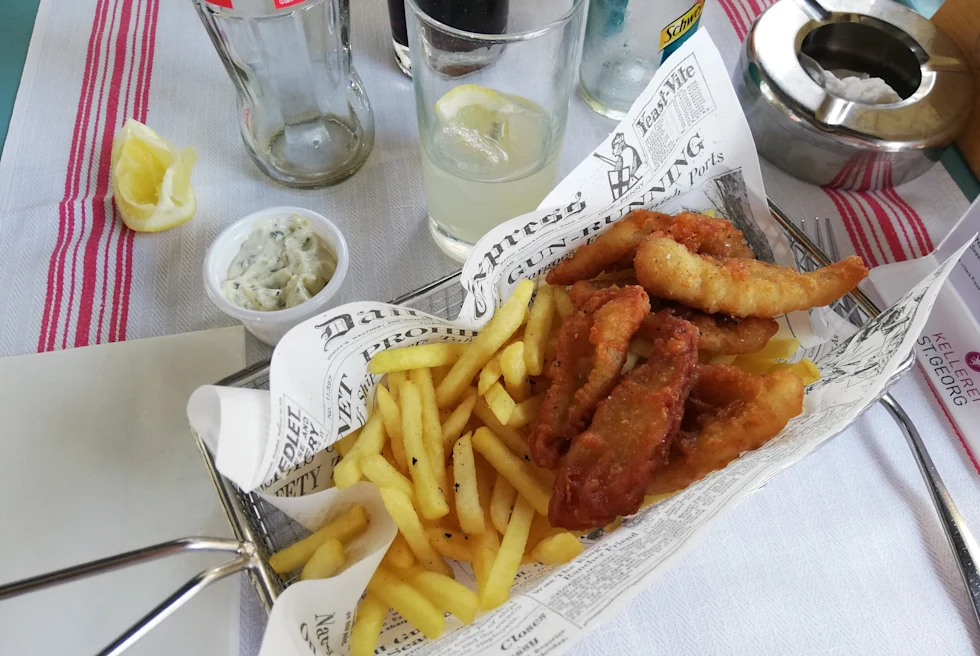 Fish and chips on a table next to lemonade.
