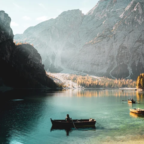 Person sits in rowboat in blue waters with mountains covered in snow in the background in Italy