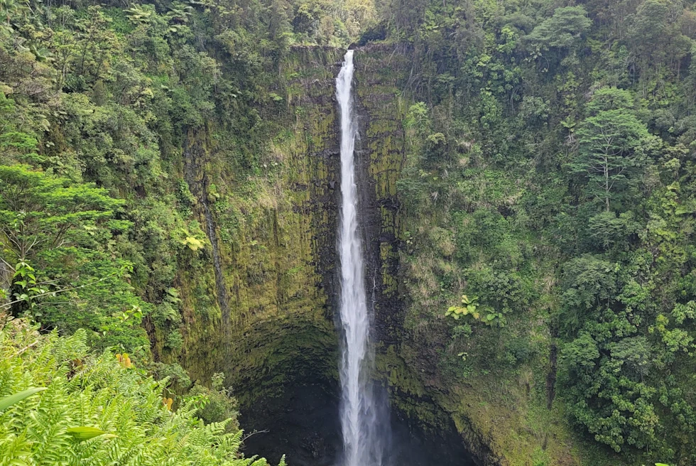Waterfall flowing down green mountain with clouds in the sky during daytime