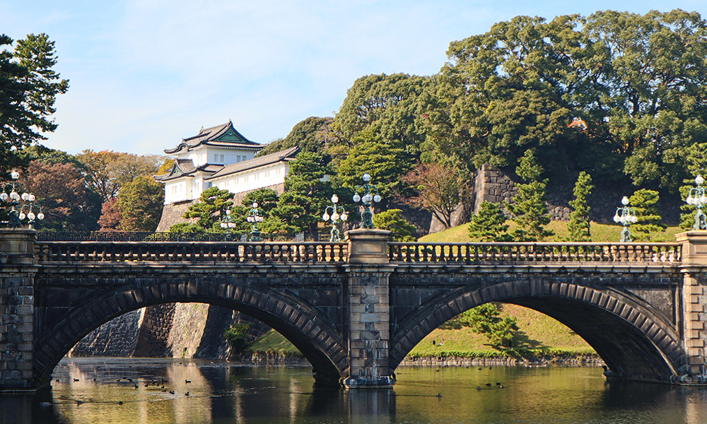 bridge in Japan with temples and tall green trees with hills and a lake