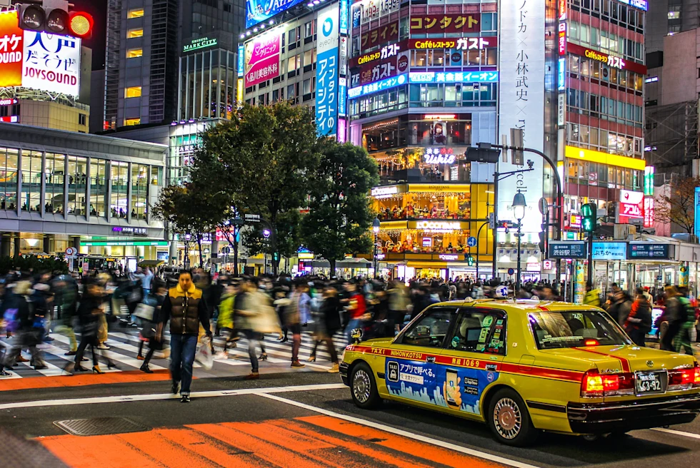 Pedestrians crossing busy crosswalk with yellow taxi and lit up buildings at night