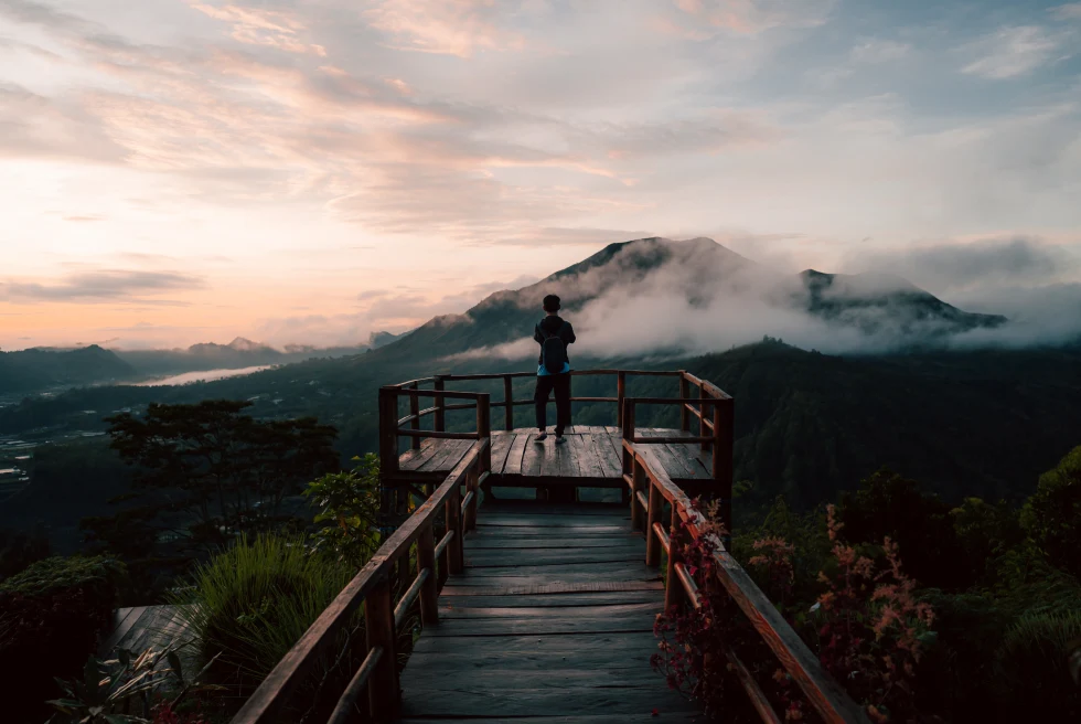 person standing on platform looking out over mountains with clouds