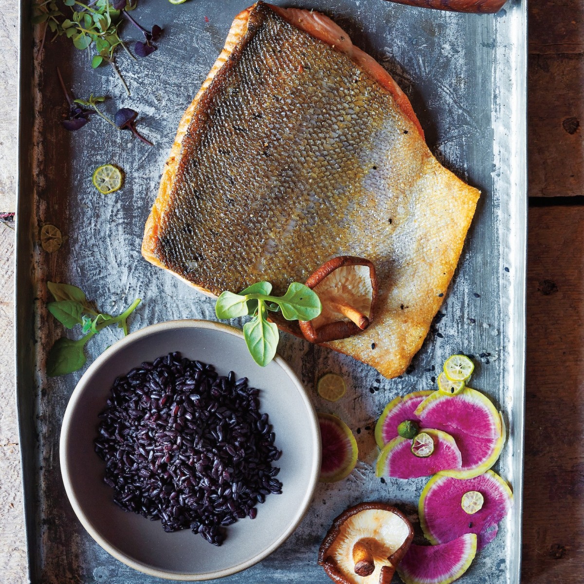 aerial view of a slab of salmon with a bowl of black rice and thinly sliced pink radishes