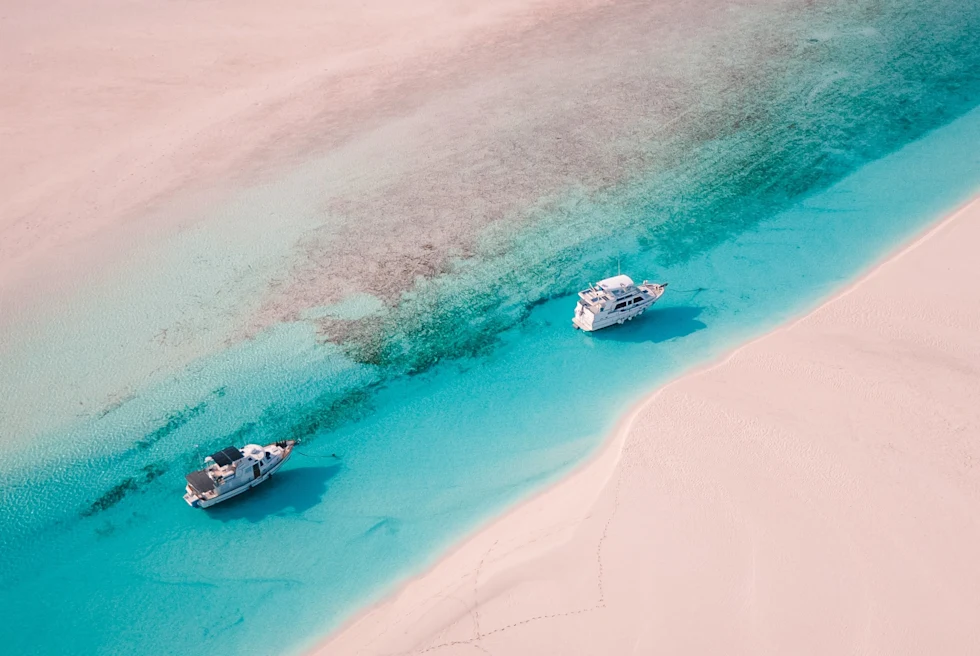 An aerial view of beach with clear blue water and boats.