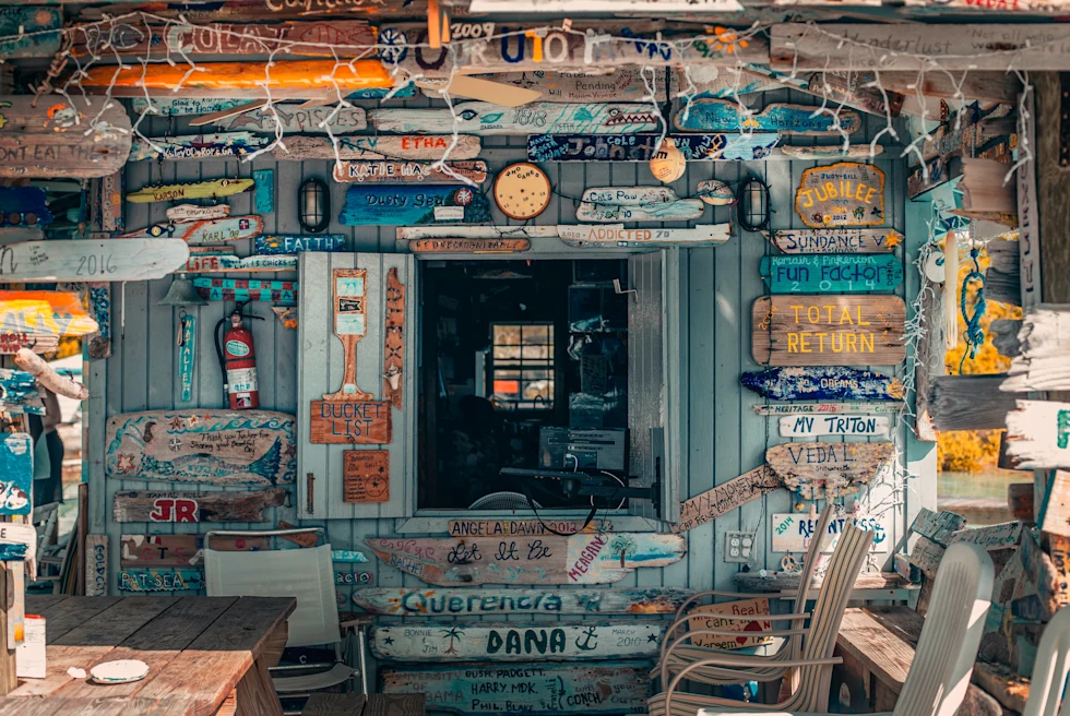 blue wall in shack with colorful beach signs white chairs string lights and wooden tables in Bahamas