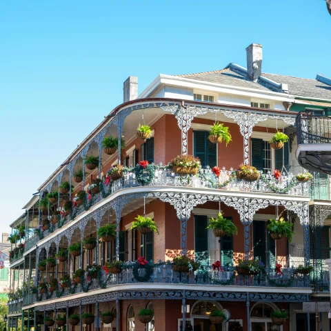 The corner of a three-story building in New Orleans with balconies and hanging plants.