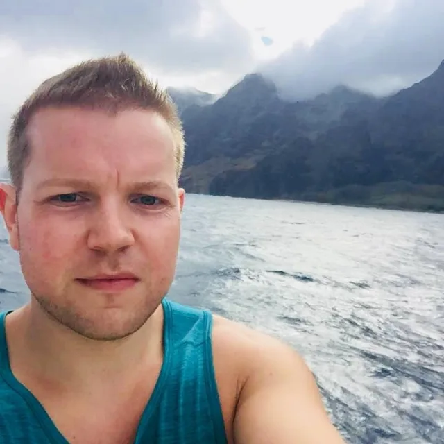Travel Advisor Jason Abrahamson in a blue tank top with an ocean and mountain backdrop.