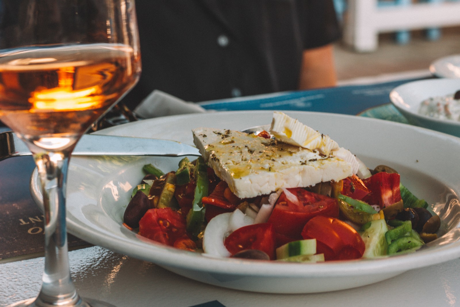 A Greek salad with tomatoes, cucumbers and feta accompanied with rose wine. 