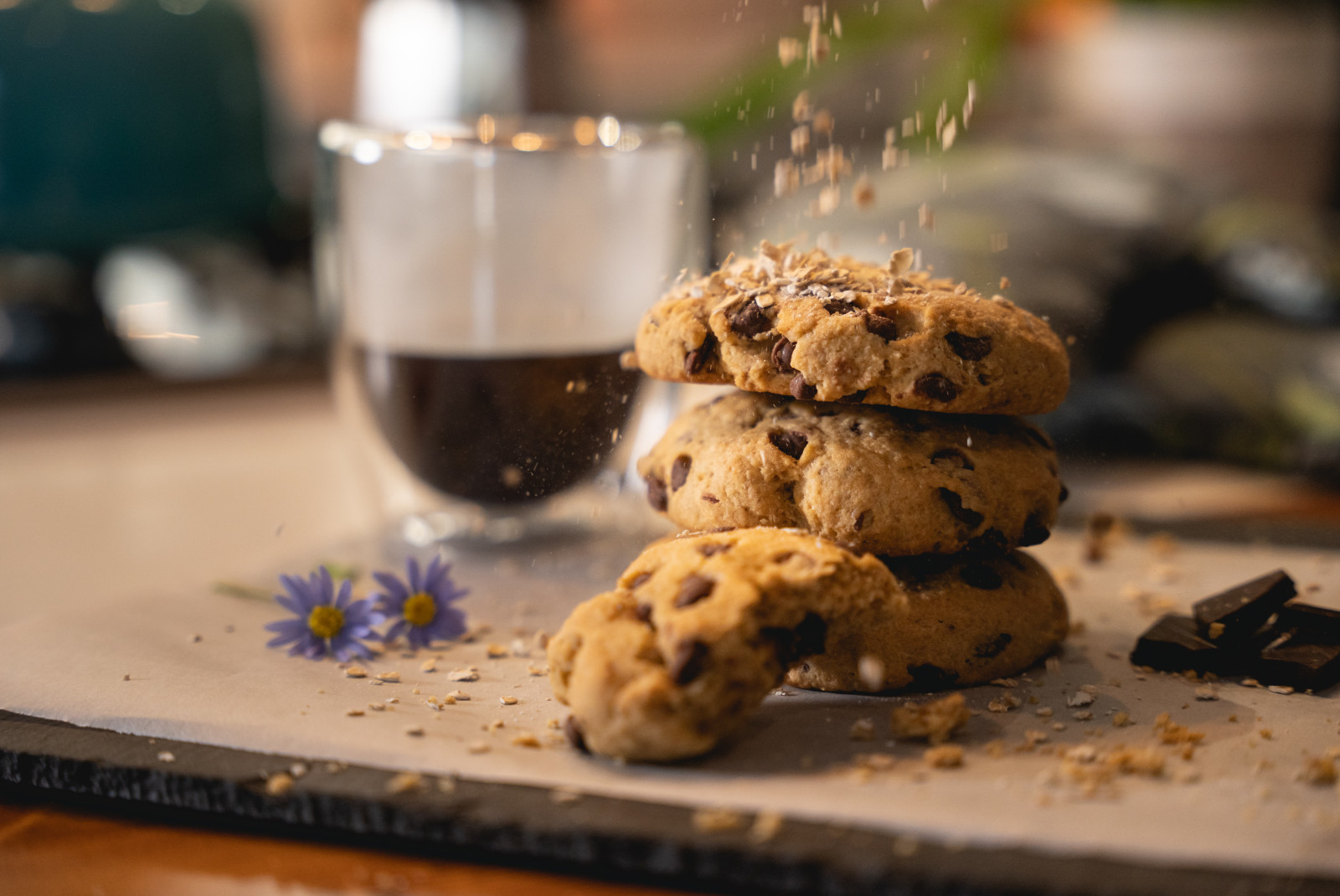 A stack of chocolate chip cookies on a plate with purple flowers and warm beverage