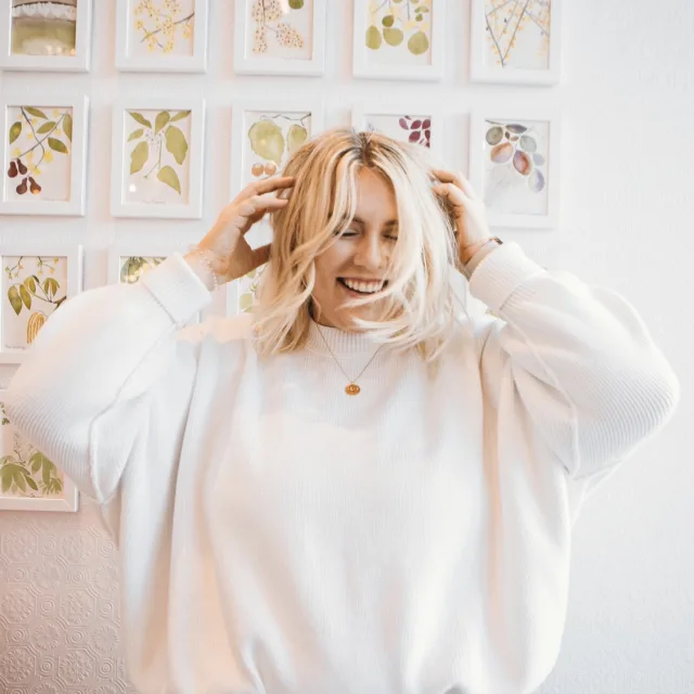 woman wearing a white sweater with a wall of art in the background