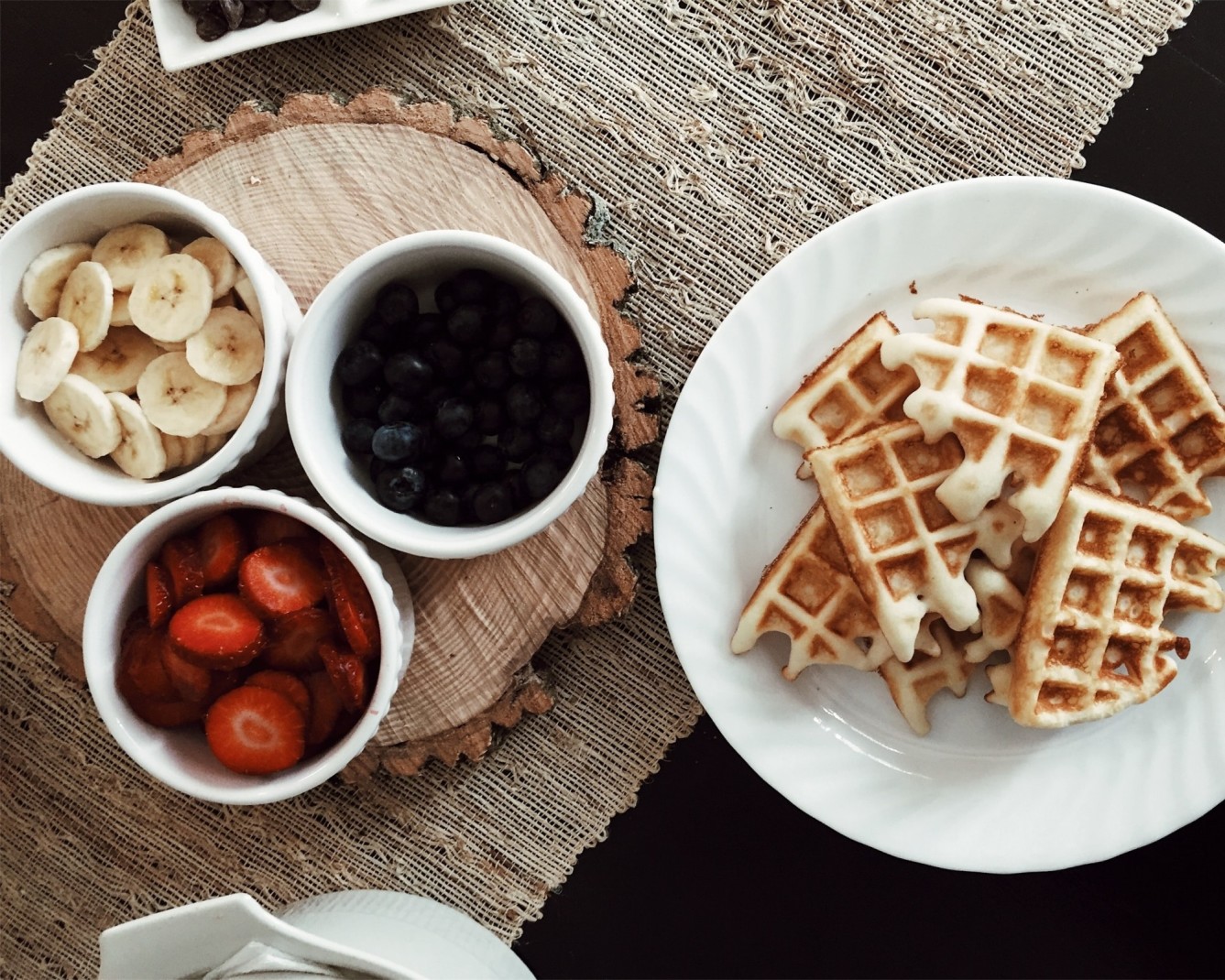 Breakfast waffles, bananas, strawberries and blueberries on a wooden table with runner. 