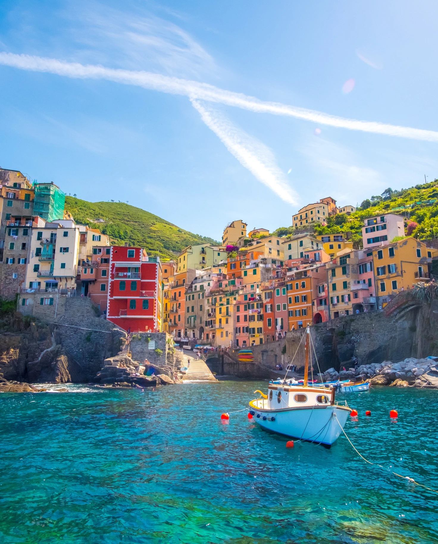Orange, yellow and blue colorful houses sitting on a rocky cliff overlooking a blue ocean with white boats in Cinque Terre, Italy.