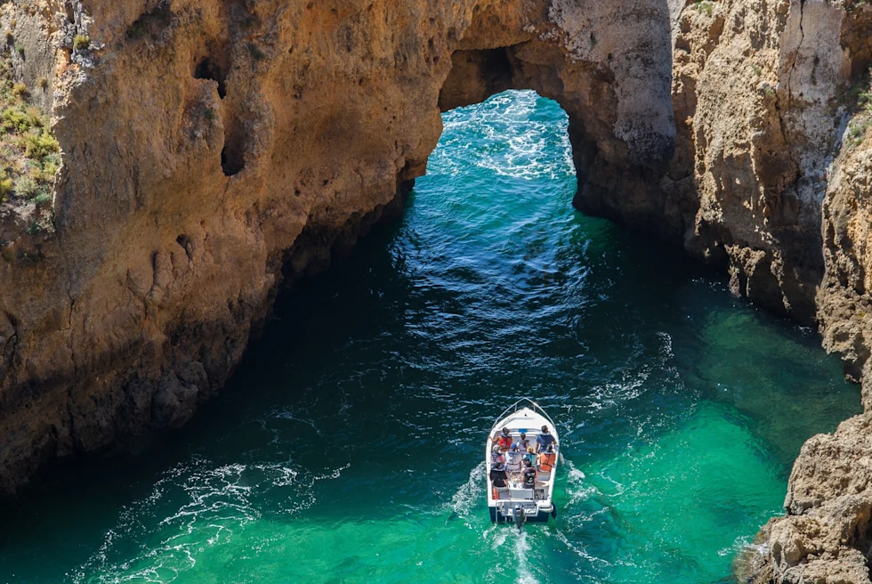 small boat cruises underneath a natural opening in stone