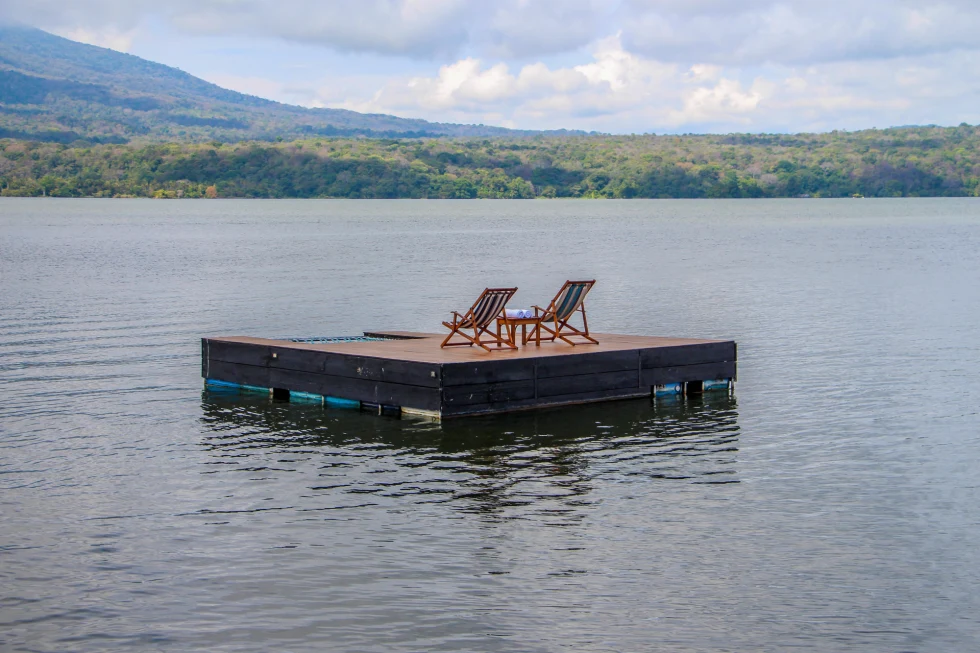 two wooden lounge chairs on a dock on calm water