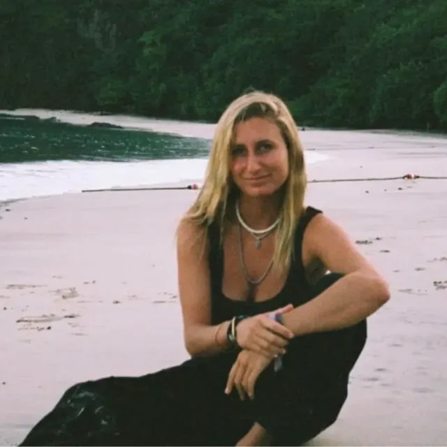 Travel advisor Lindsey Falack sitting on a secluded beach wearing black.