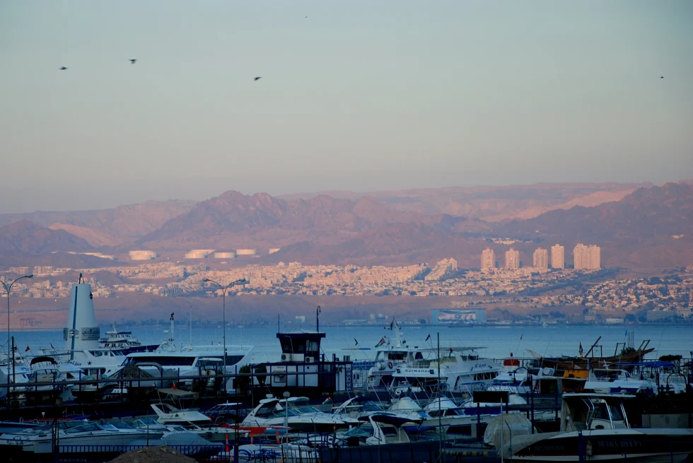 Boats parked along the water in Aqaba, Jordan with red hills and buildings in the background