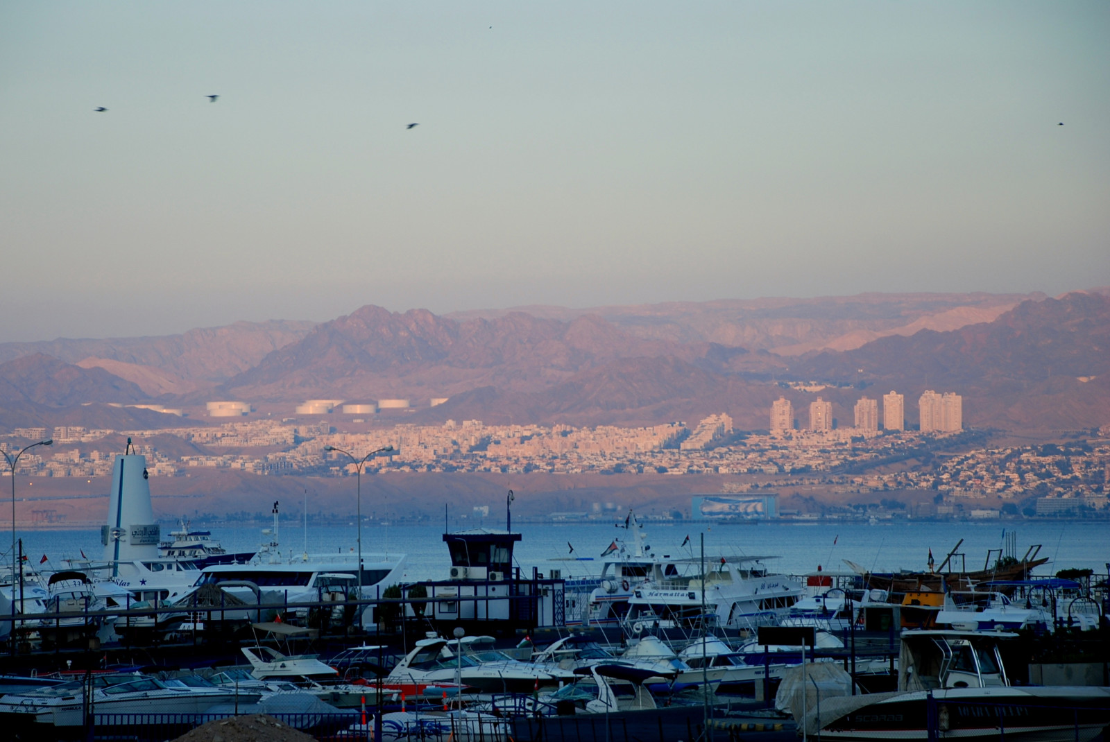Boats parked along the water in Aqaba, Jordan with red hills and buildings in the background