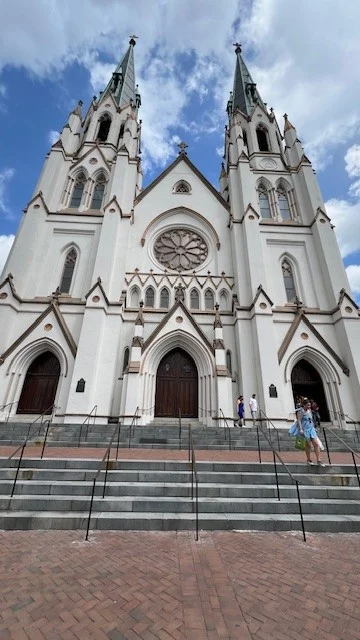 The the Cathedral of Basilica of St John the Baptist, a large white church with brown trim, on a sunny day.