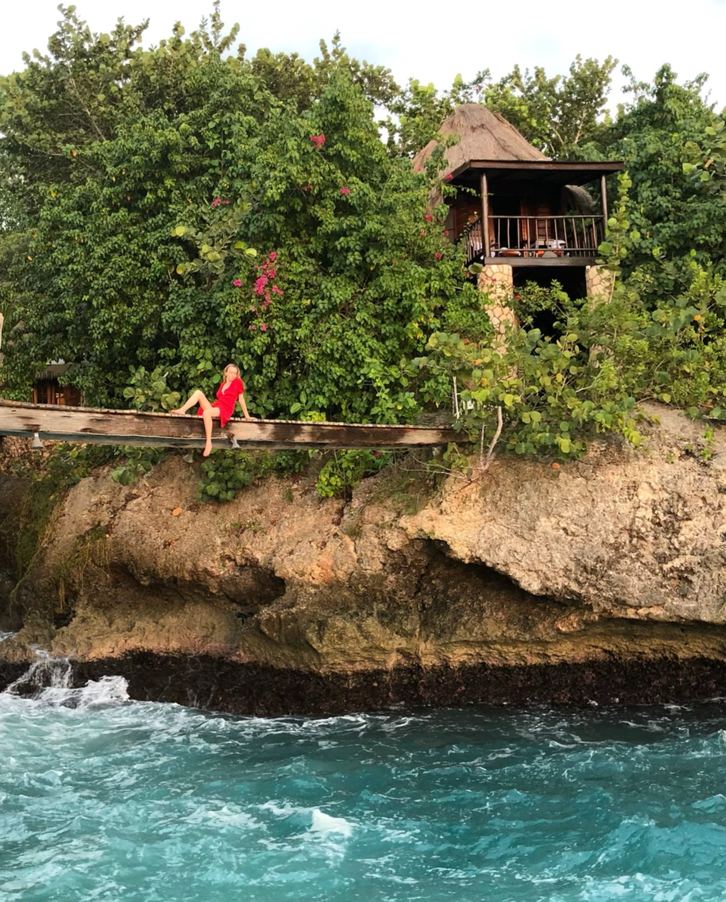 Woman wearing red and sitting on the bridge over the ocean at Tensing Pen in Negril, Jamaica