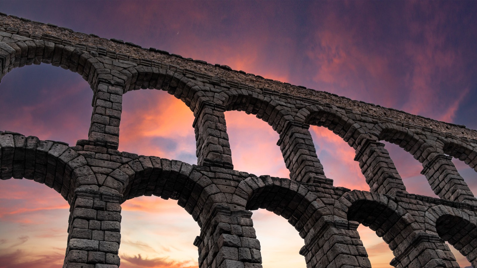 Stone arches of Segovia in Madrid, Spain with a pink and yellow sunset in the sky