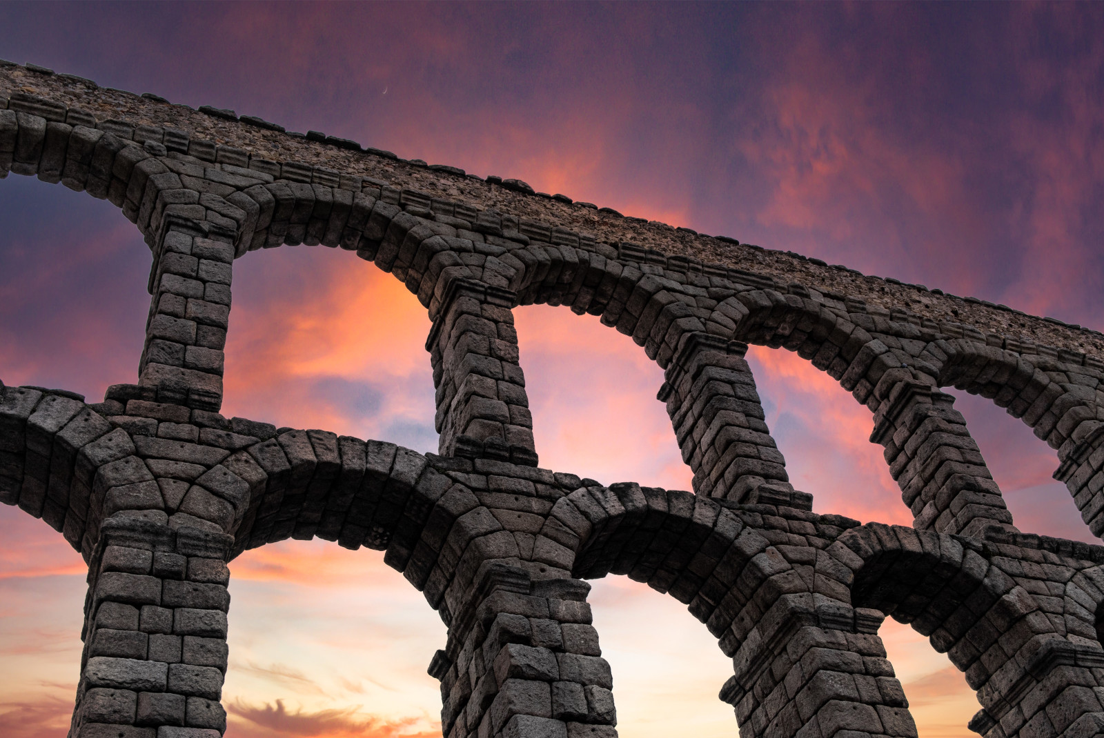 Stone arches of Segovia in Madrid, Spain with a pink and yellow sunset in the sky