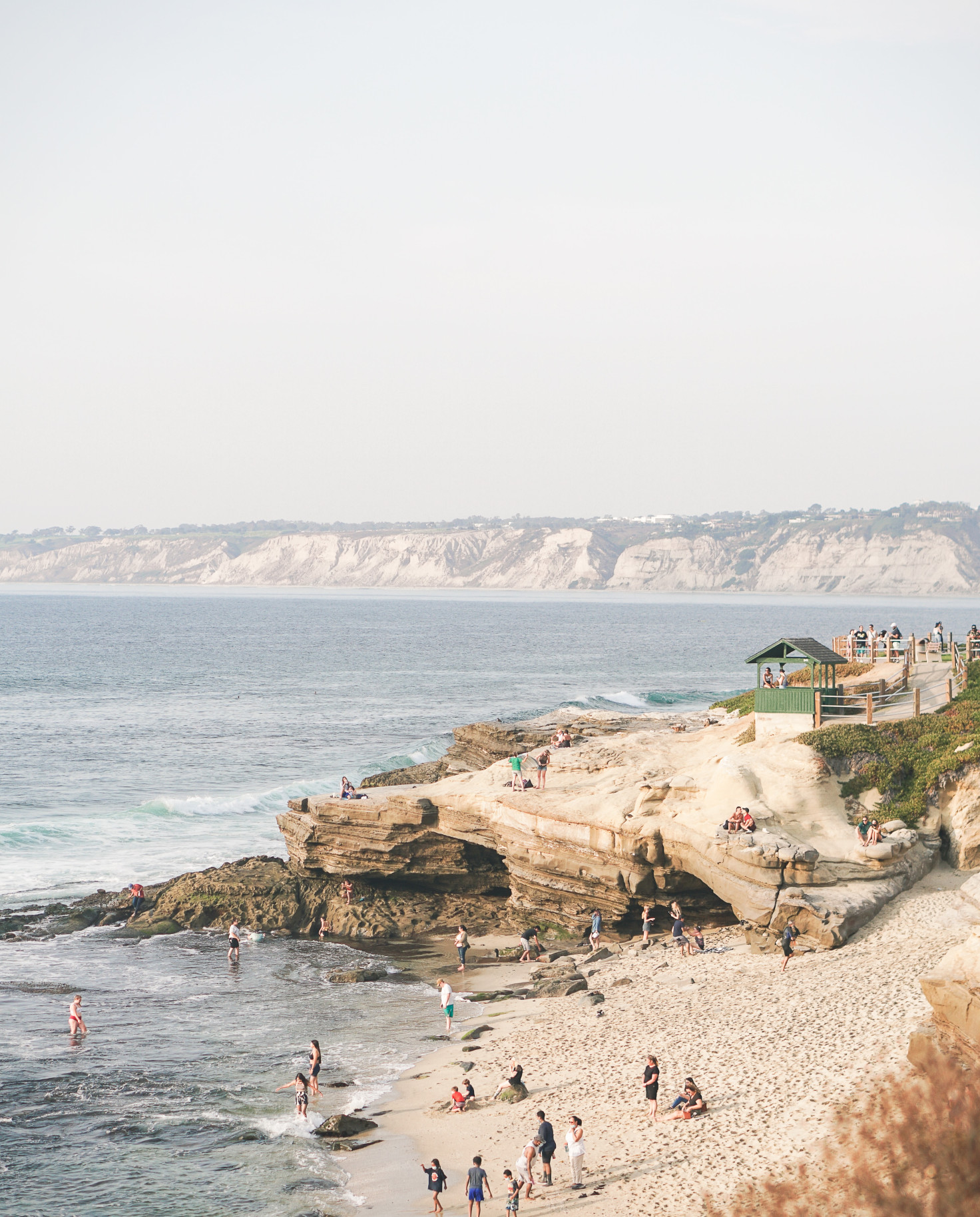 People stand on the sand and in the water on La Jolla Cove in San Diego