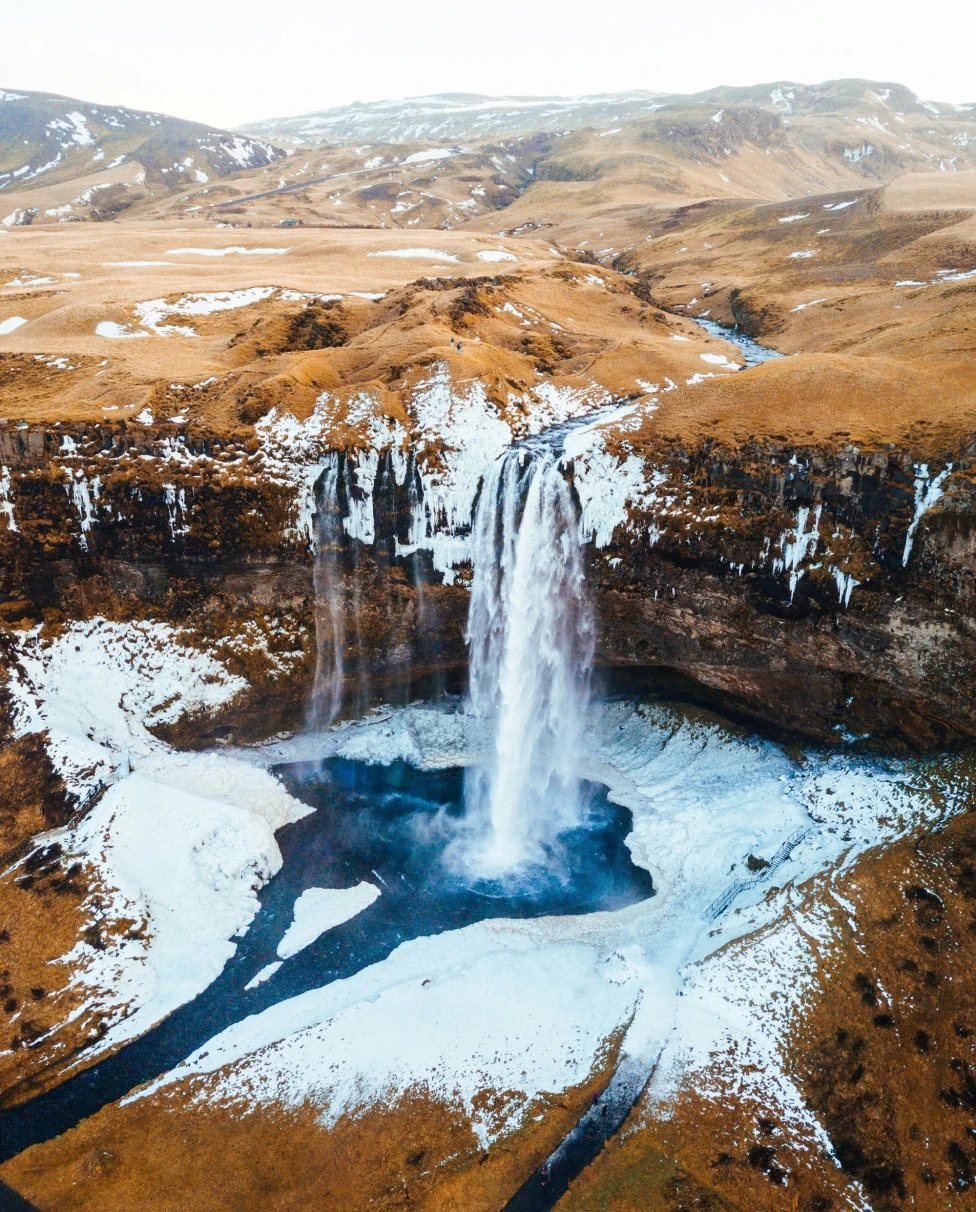 An aerial photo of a frozen waterfall near the mountains.