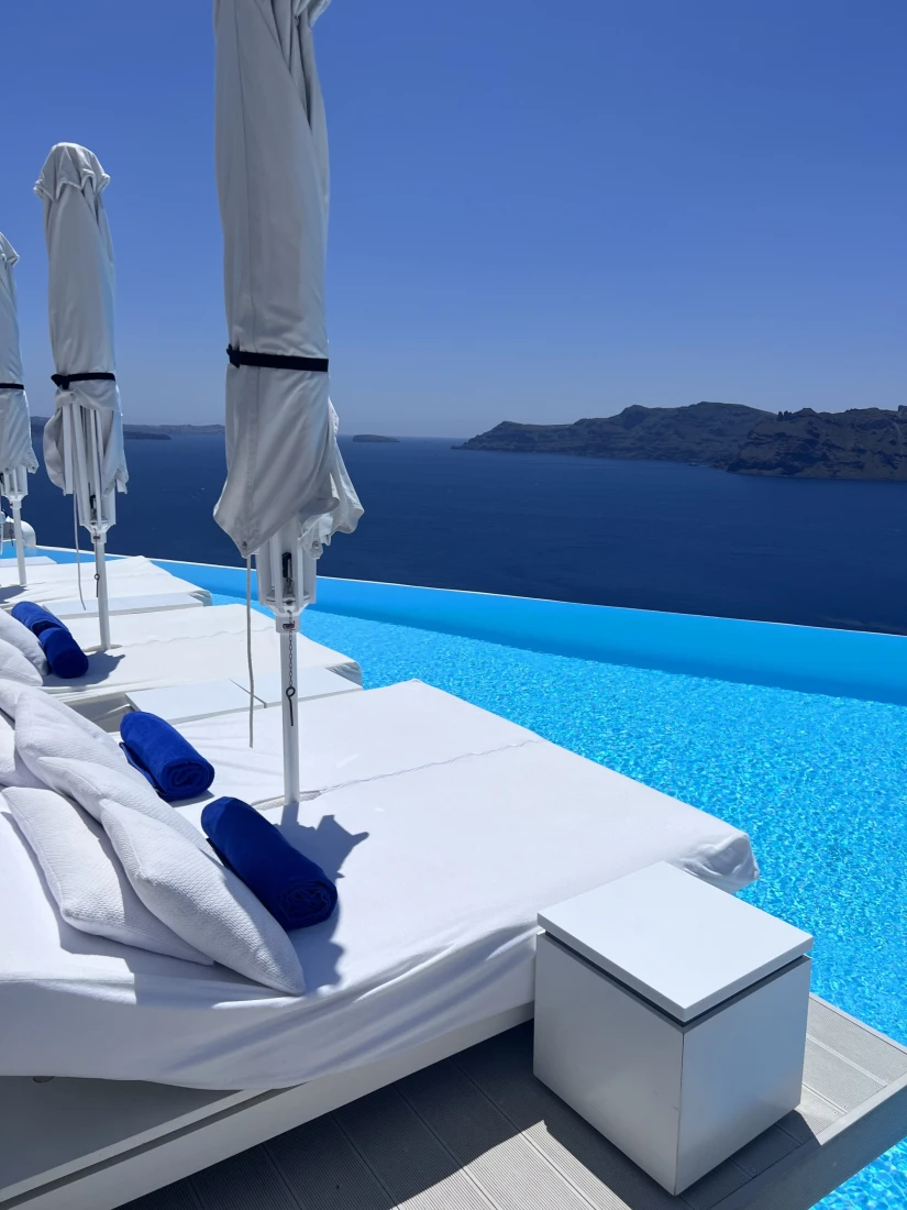 white loungers beside a blue cliffside infinity pool