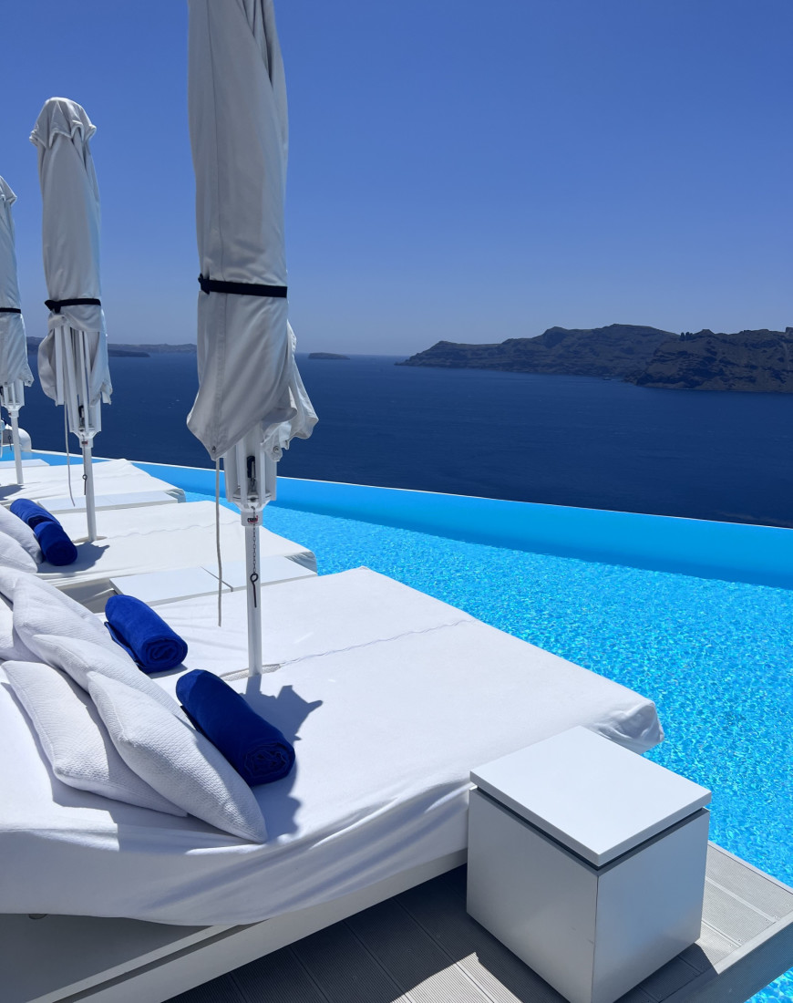 white loungers beside a blue cliffside infinity pool