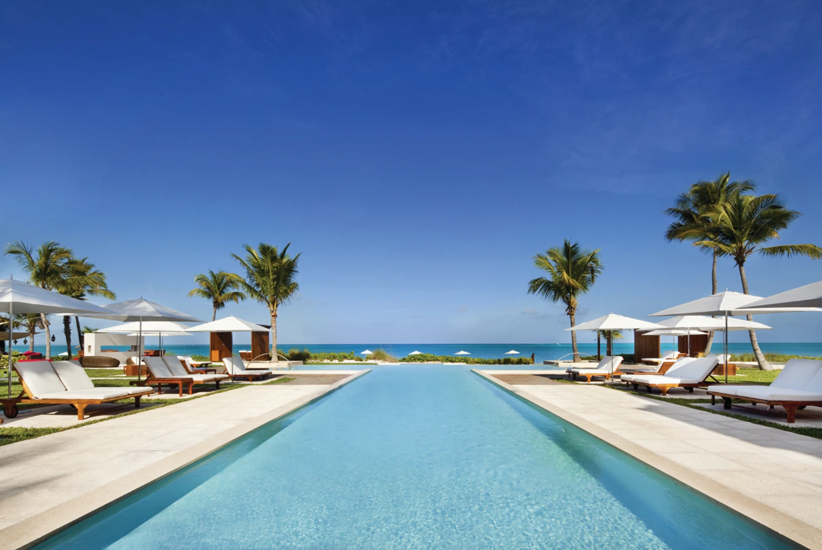 A poolside with white lounge chairs and umbrellas. 
