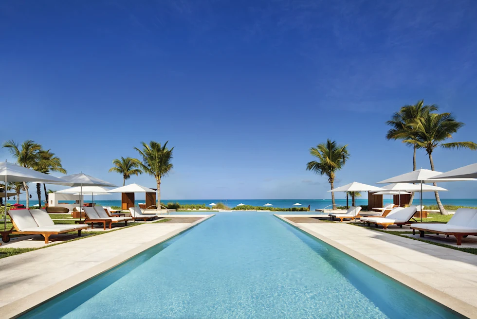 A poolside with white lounge chairs and umbrellas.