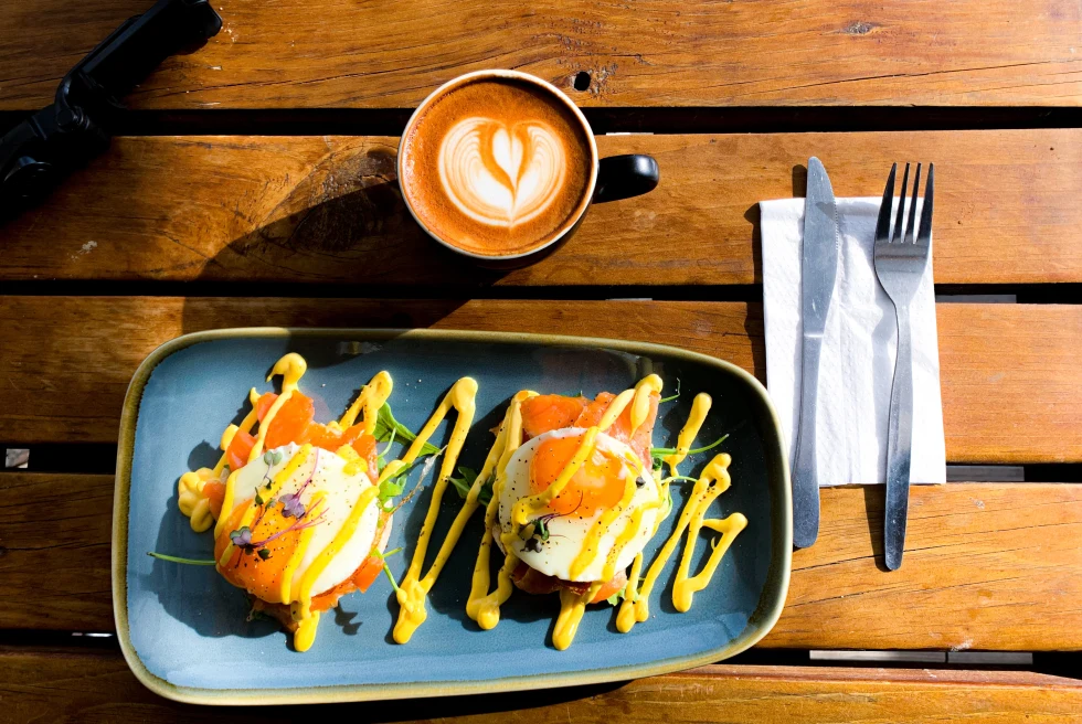 Eggs and sauce on a blue plate next to a mug of coffee on a wooden table