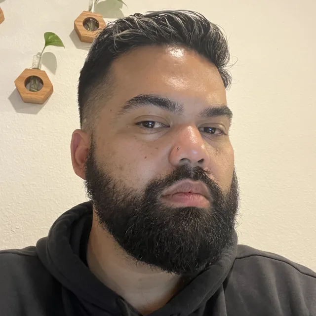 Travel Advisor Daniel Maquindang in a black sweatshirt in front of a white wall with orange and green plants in the background.