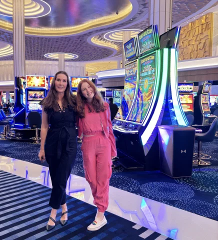 A woman in a black jumpsuit and a woman in a pink jumpsuit standing on a casino floor.
