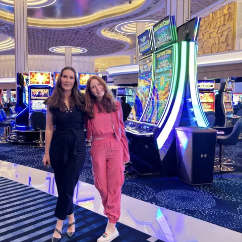 A woman in a black jumpsuit and a woman in a pink jumpsuit standing on a casino floor.