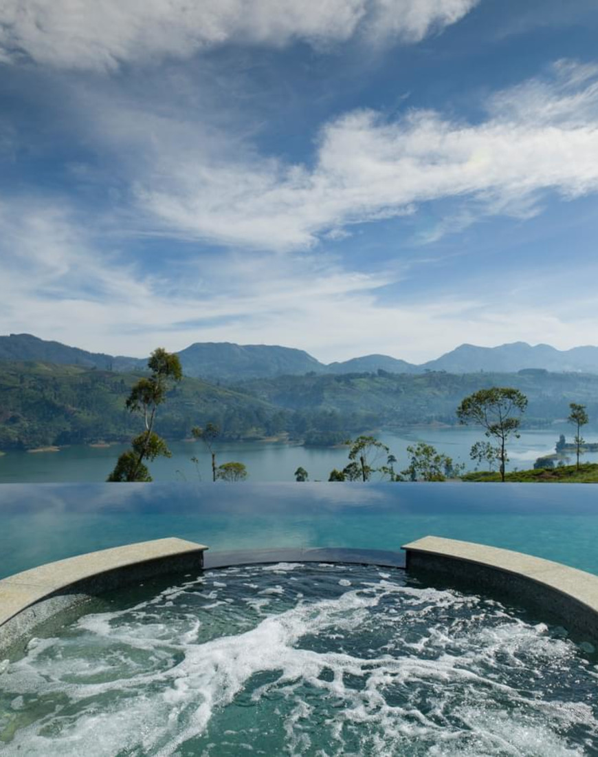 a hot tub within an infinity pool overlooking a lake surrounded by greenery