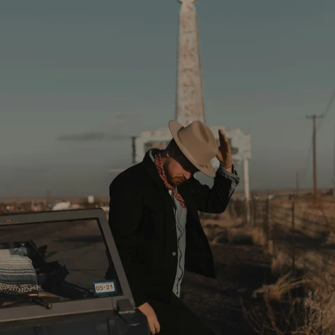A picture of a man holding tipping a cowboy hat in front of a Texan monument. 