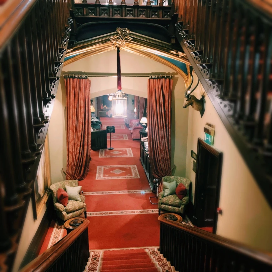 A view of stairs leading downward to luxurious red carpeting, curtains and lavish woodwork. 