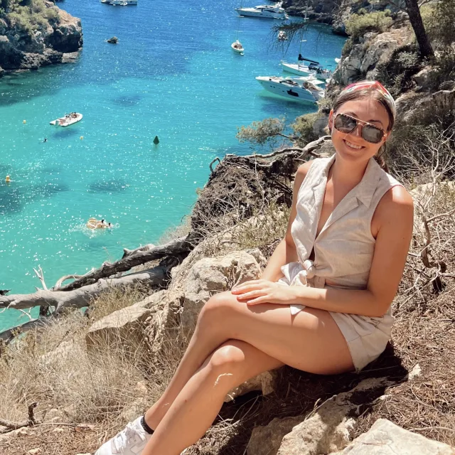 travel advisor Abby Kulwicki in sunglasses smiling on a trail overlooking a turquoise ocean lagoon