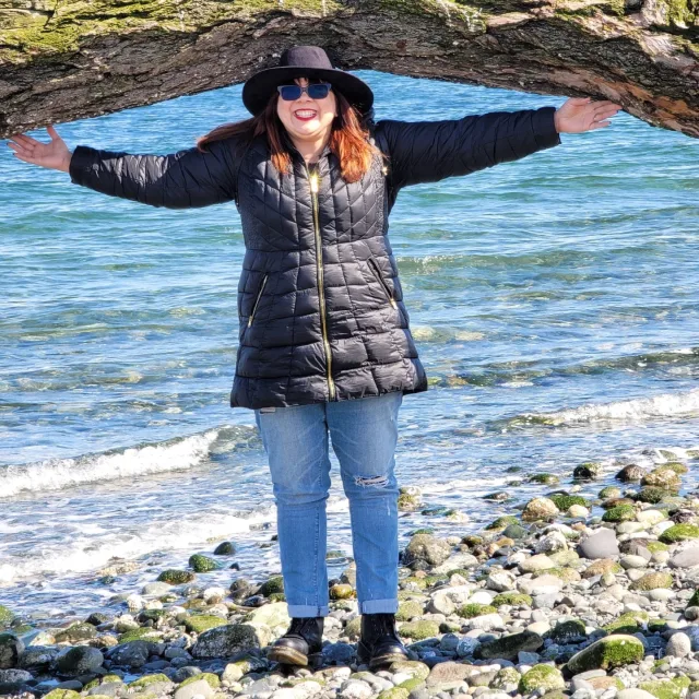 Travel Advisor Venus Sherrill standing under a moss covered tree on rocks with water in the background.