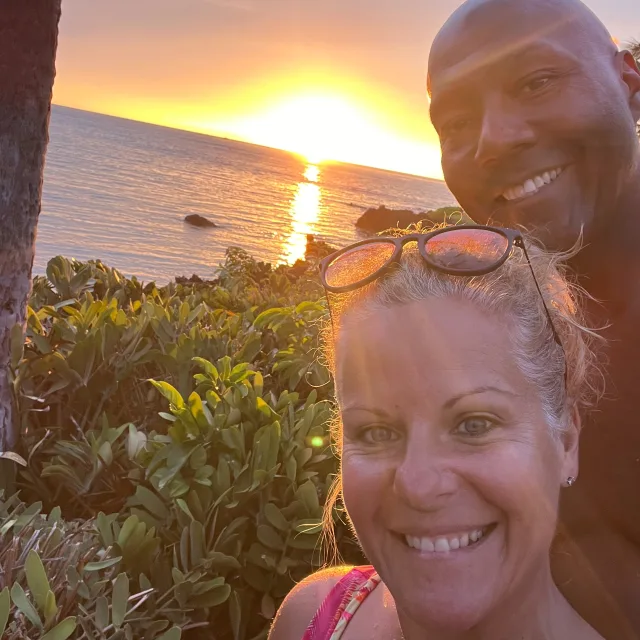 Travel Advisor Amy LaGrow-Rogers with her husband in front of a beach at sunset.