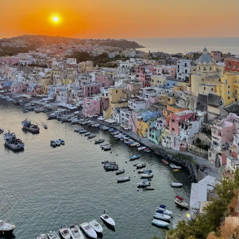 A picture of a beautiful coastline with colorful houses and boats in the water at sunset. 