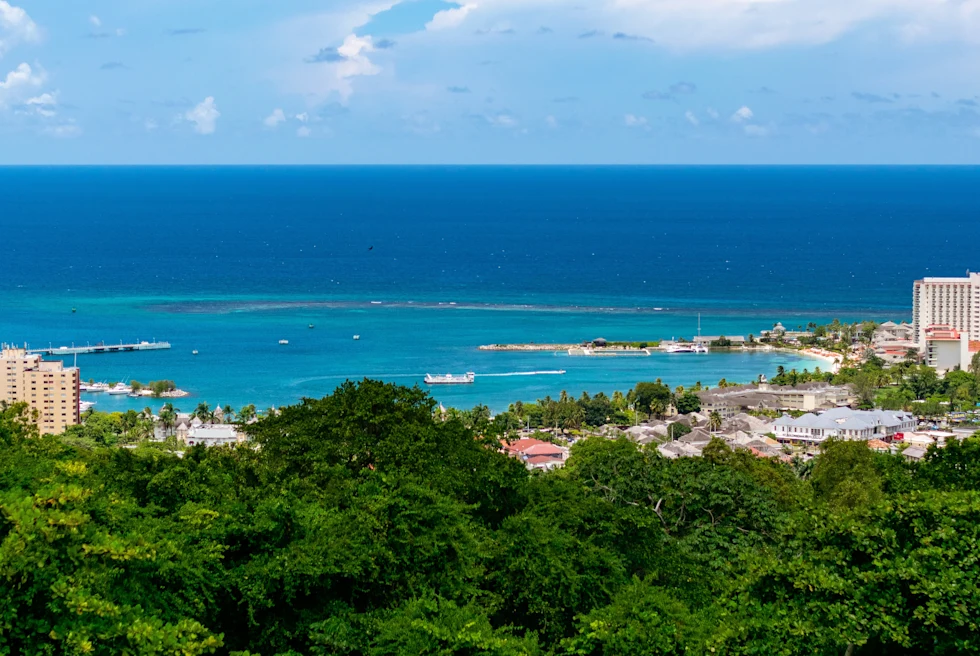 Green trees along the coast in Jamaica with hotels and blue ocean in the background
