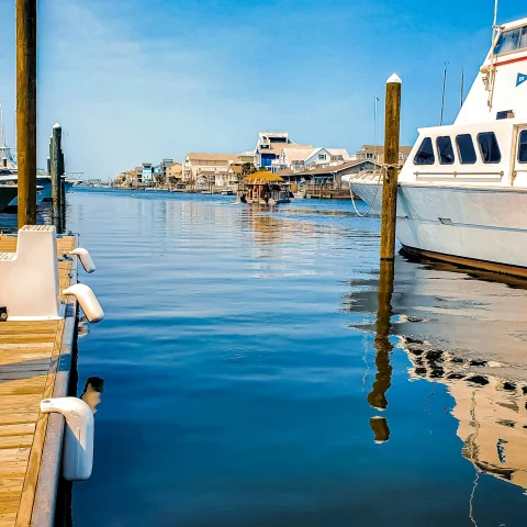 The image depicts a tranquil dockside setting with clear skies and calm waters, featuring a wooden dock and a white boat moored to the side.