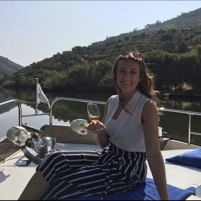 woman in a white tank and striped pants sits on a boat holding a wine glass