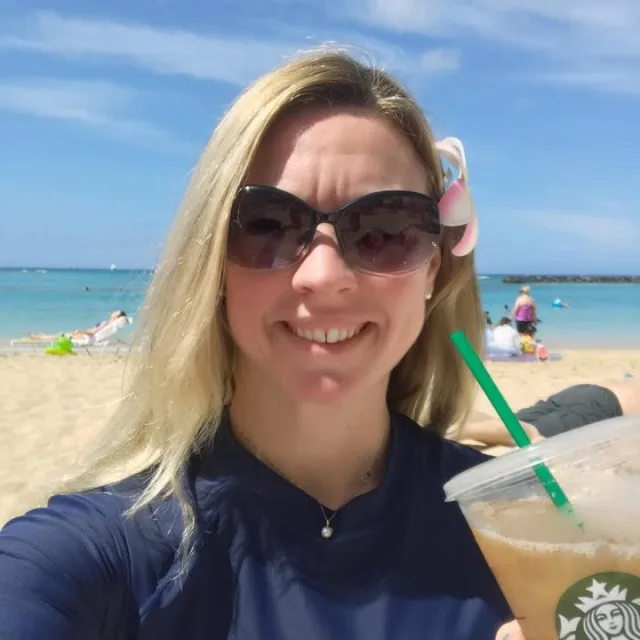 Travel Advisor Karri Long in a blue shirt on a beach holding a Starbucks coffee.