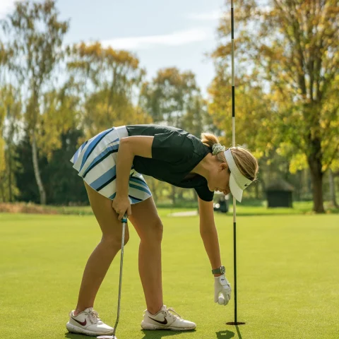 A picture of a woman putting a golf ball on the course.