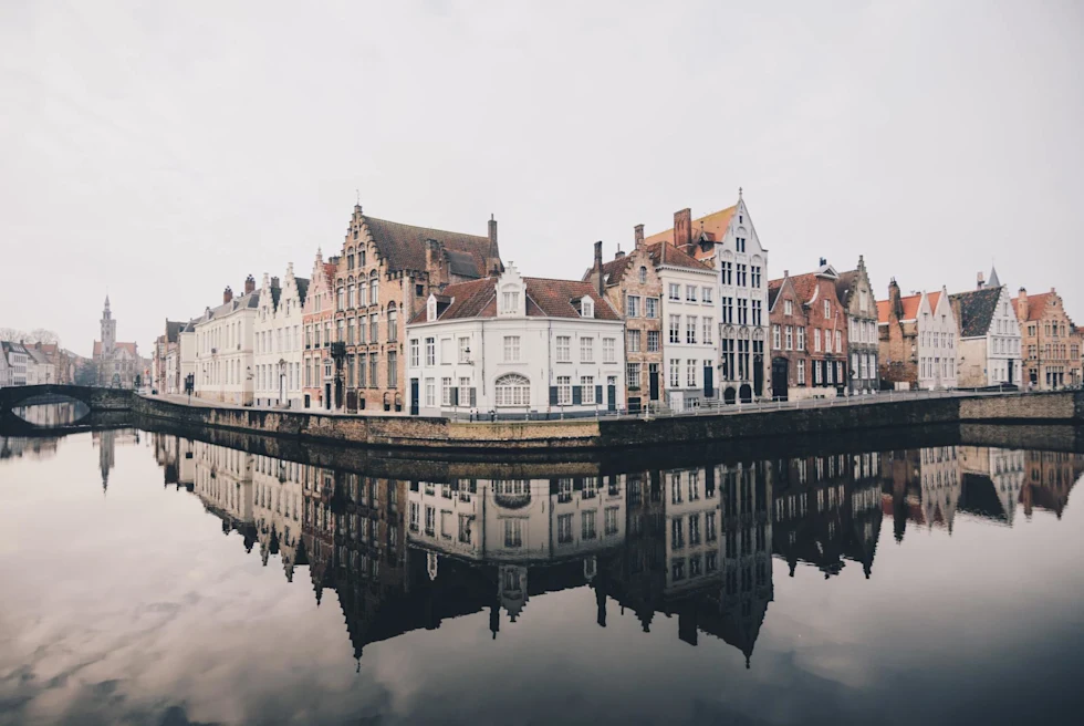 the corner of a city reflecting into a placid gray river 