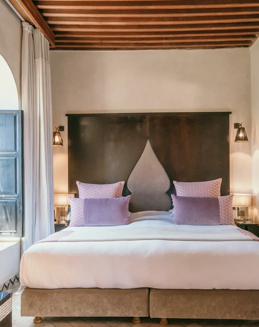 a white bed with a tall headboard and purple pillows