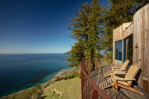 A sleek wooden terrace with lounge chairs and a view of the Pacific